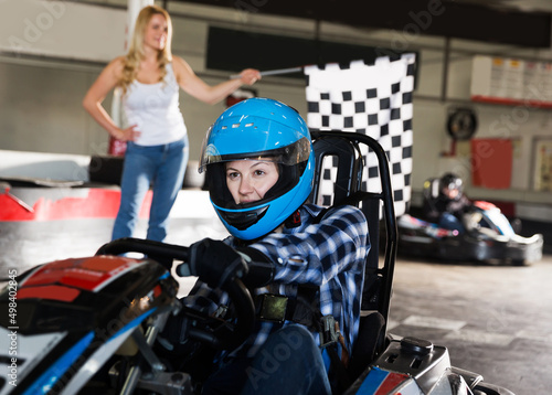 Youn woman driving sport car for karting in sport club, woman with race flag on background