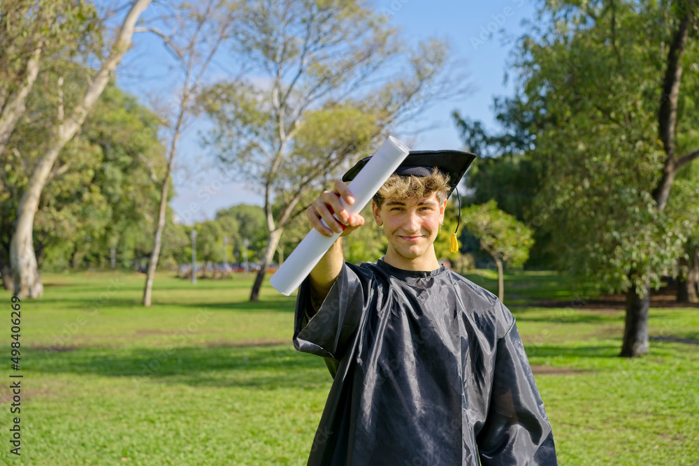 Young recent graduate boy, dressed in cap and gown, showing off his ...