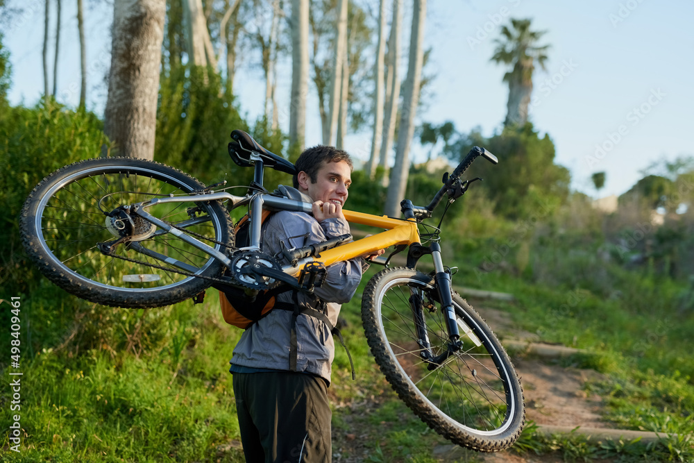 Fototapeta premium Guess Im carrying my bike from here. Rearview shot of a handsome male athlete carrying his bike while mountain biking through the forest.
