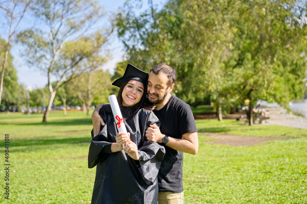 Young girl recently graduated, dressed in cap and gown, with her degree in her hands, celebrating with her family on the university campus. Very happy expression, achievement, beginning of a new stage Young girl recently graduated, dressed in cap and gown, with her degree in her hands, celebrating with her family on the university campus. Very happy expression, achievement, beginning of a new stage