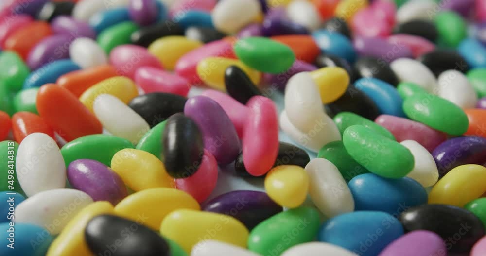 Video of close up of multi coloured sweets falling over blue background Video of close up of multi coloured sweets falling over blue background