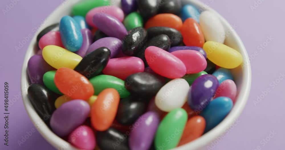 Video of close up of multi coloured sweets in bowl over purple background Video of close up of multi coloured sweets in bowl over purple background