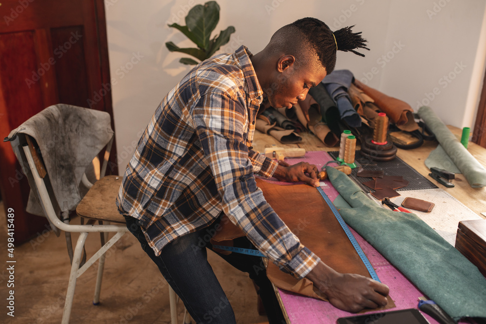 © Wavebreak Media - Side view of african american young craftsman measuring leather at workbench in workshop © Wavebreak Media - Side view of african american young craftsman measuring leather at workbench in workshop