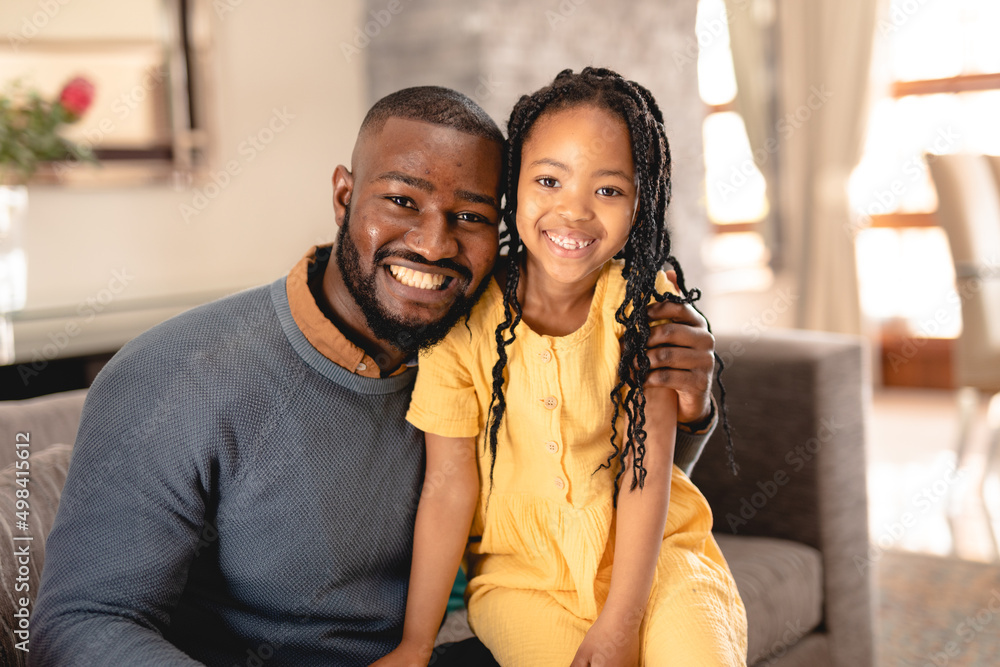 Portrait of smiling african american man sitting with arm around daughter on sofa in living room Portrait of smiling african american man sitting with arm around daughter on sofa in living room