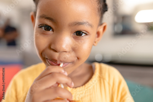 Close-up portrait of cute african american girl eating lollipop at home photo