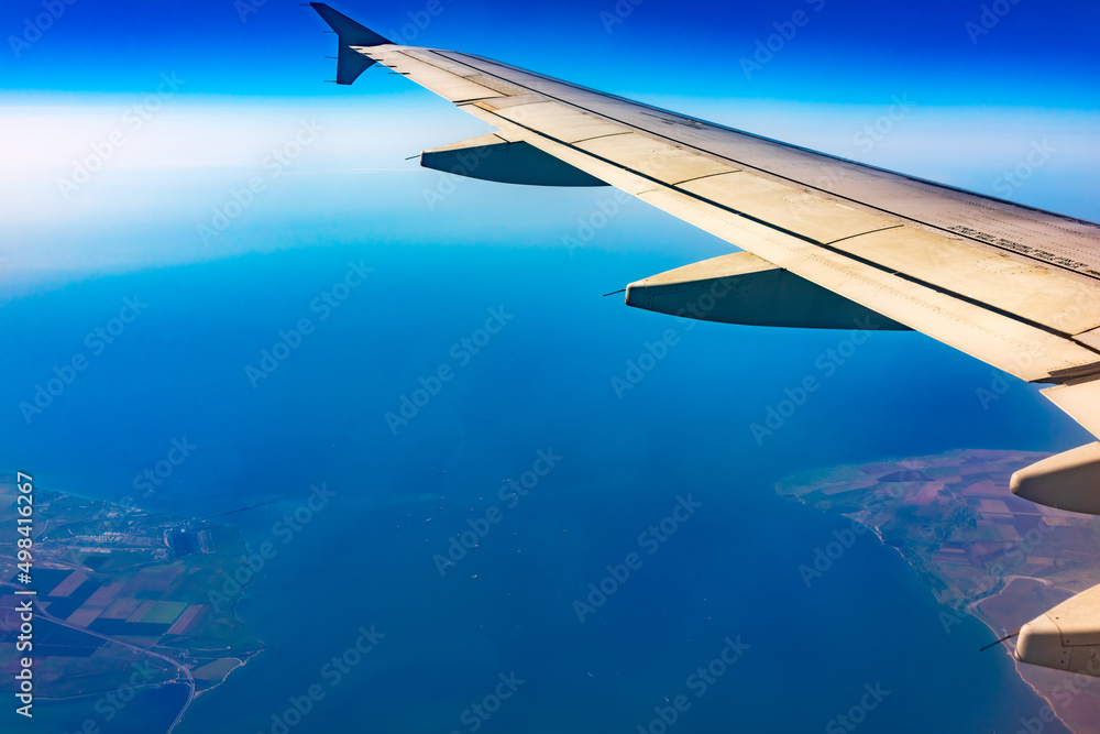View from the airplane window at a beautiful blue clear sky, earth, sea and the airplane wing View from the airplane window at a beautiful blue clear sky, earth, sea and the airplane wing
