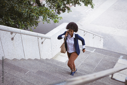 African american mid adult businesswoman talking on phone while rushing steps in city photo