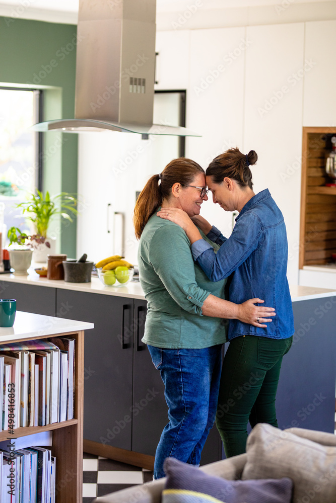 Romantic mature caucasian lesbian couple standing face to face by kitchen island at home Romantic mature caucasian lesbian couple standing face to face by kitchen island at home