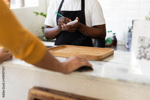 Midsection of african american barista taking order from customer at counter in cafe photo