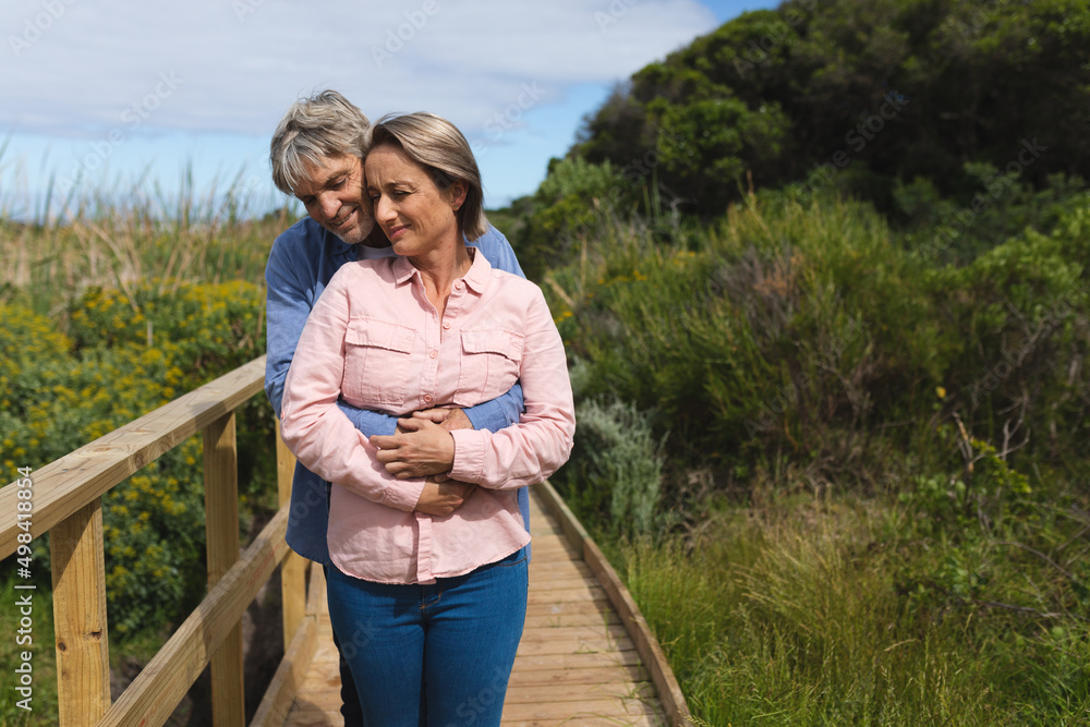 Romantic caucasian mature couple embracing while standing by railing on boardwalk during weekend Romantic caucasian mature couple embracing while standing by railing on boardwalk during weekend