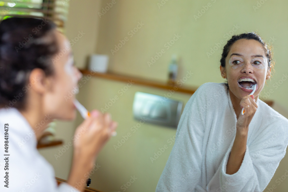 Happy biracial young woman brushing teeth in front of mirror in bathroom Happy biracial young woman brushing teeth in front of mirror in bathroom
