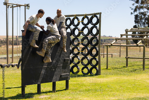 Two diverse male soldiers helping male african american soldier to climb wooden wall at boot camp photo