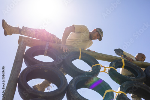 Two diverse male soldiers climbing a tire wall during obstacle course at boot camp photo