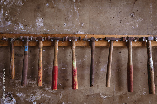 Various hammers hanging side by side on hook rack mounted on wall in industry photo