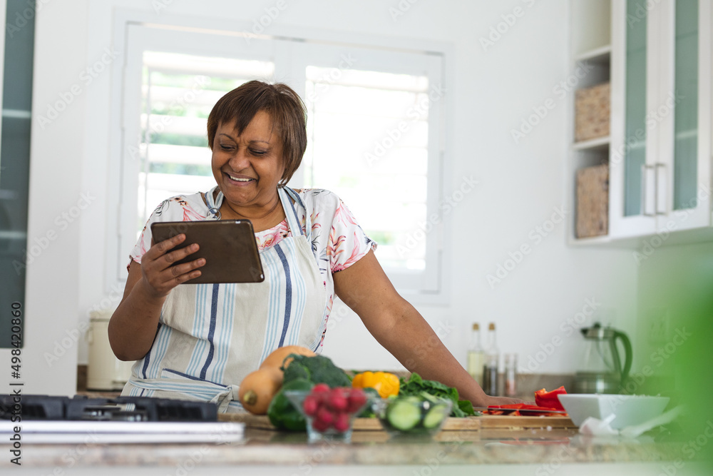 Smiling senior woman watching online recipe on digital tablet while cooking food in kitchen at home Smiling senior woman watching online recipe on digital tablet while cooking food in kitchen at home