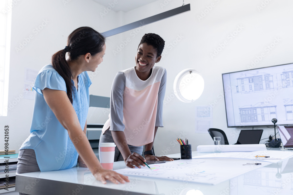 Multiracial female architects smiling while discussing over blueprint in meeting at office Multiracial female architects smiling while discussing over blueprint in meeting at office