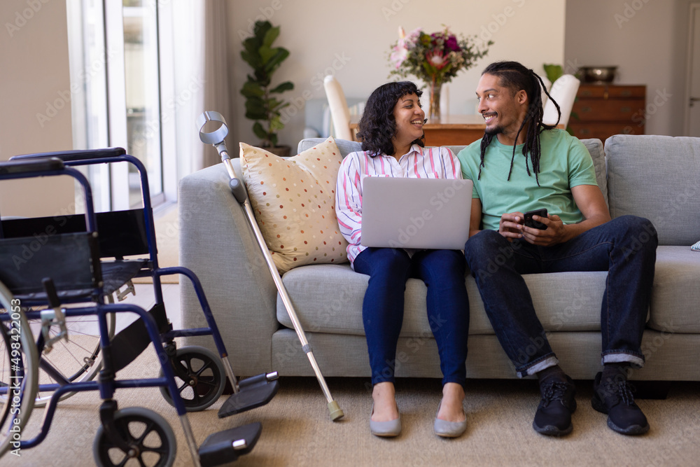 African american man and disabled wife using laptop sitting together on the couch at home African american man and disabled wife using laptop sitting together on the couch at home