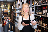 Portrait of confident middle aged woman owner of wine store offering to buy bottled wine..