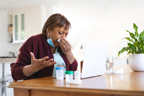 Senior woman taking online doctor consultation on laptop while suffering from cold and flu photo