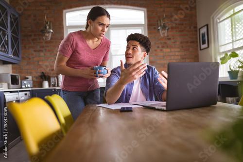 Worried biracial couple discussing over expenditure through laptop in kitchen at home
