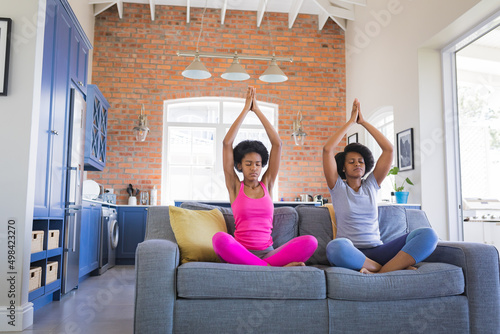 African american mother and daughter meditating with hands clasped on sofa at home photo