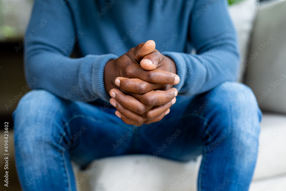 Midsection of african american man sitting on sofa with intertwined fingers at home Midsection of african american man sitting on sofa with intertwined fingers at home