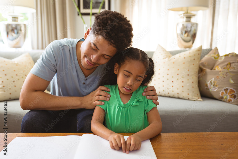 Biracial blind girl touching braille while reading book by father in living room at home Biracial blind girl touching braille while reading book by father in living room at home