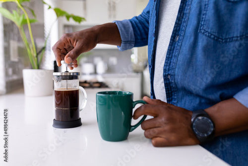 Midsection of senior african american man using french press holding coffee mug at kitchen counter photo