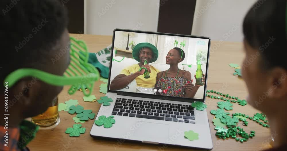 Smiling african american couple with beer wearing clover shape items on video call on laptop Smiling african american couple with beer wearing clover shape items on video call on laptop