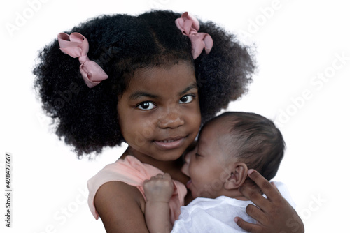Adorable African older sister cuddling with her toddler baby brother, sweet moment between a big sister and her baby brother, against white background, looking at camera