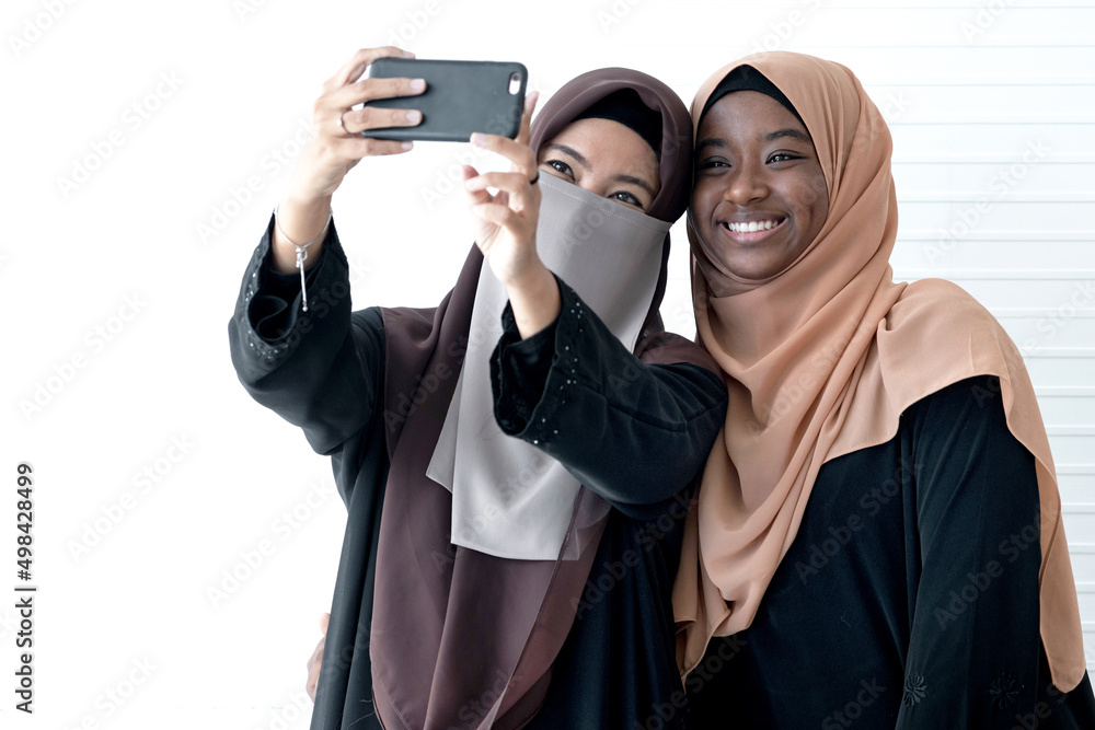 Two Muslim female friends make a selfie, on white wall background Two Muslim female friends make a selfie, on white wall background