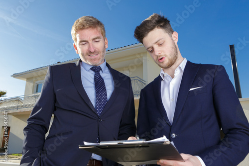 two suited men looking at clipboard outside of property photo
