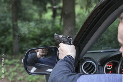 A man with a pistol takes aim from the car window.