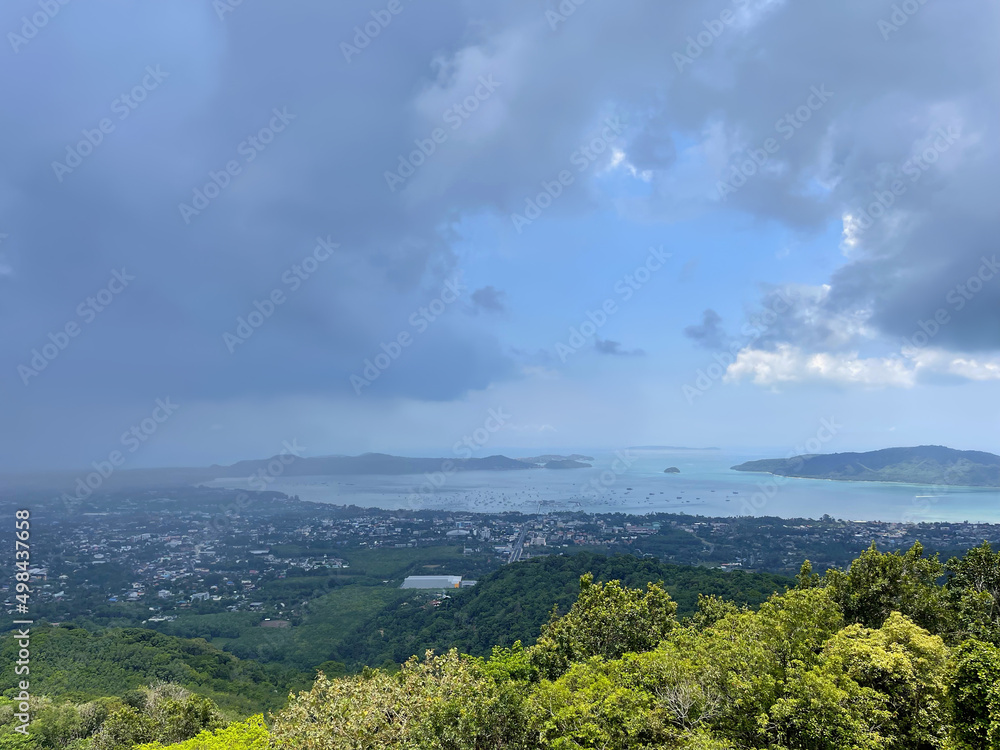 Panoramic top view of the green forest, blue sea, town, islands, and boats on the water. Summer landscape. Sky with storm clouds. Ray of sun breaks through thick clouds. Spring thunderstorm. Panorama.
