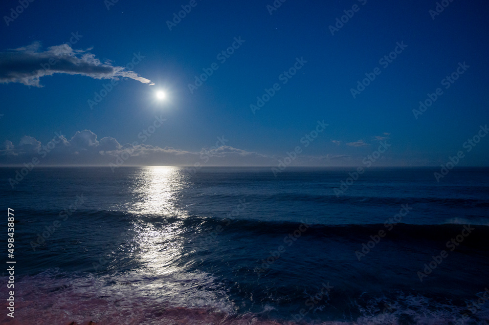 Moonlight path on water of Atlantic ocean at night on Tenerife and dark blue sky with full Moon and stars