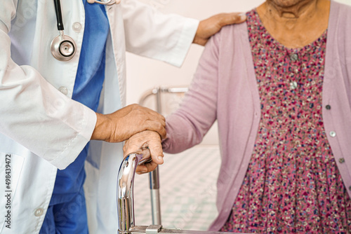 Doctor help Asian elderly woman disability patient walk with walker in nursing hospital, medical concept.