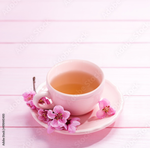 Cup of tea and spring flowers (Peach blossom) on light pink wooden table. Selective focus.