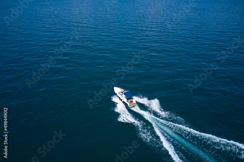Large white boat with people back view on blue water in the rays of the sun aerial view. Boat with a blue tent on the water top view. Boat motion top view. © Berg