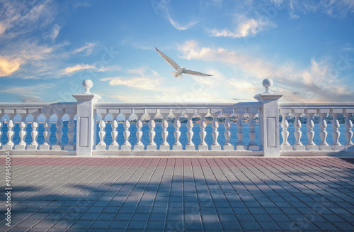 Fototapet White decorative fence with columns on the seashore and seagull in sky