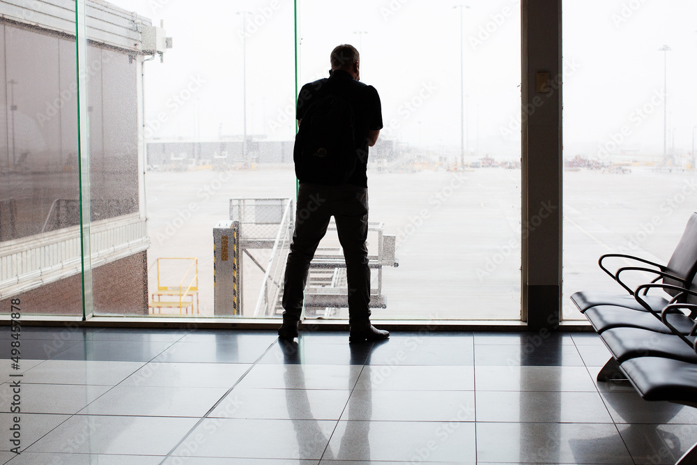 Fototapeta premium Single male figure talking on mobile phone standing in front of large window