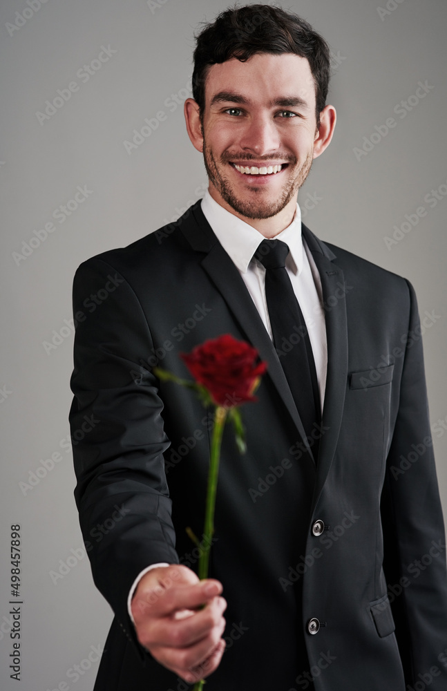 The perfect gentleman. Studio shot of a well-dressed man holding a red rose against a gray background. The perfect gentleman. Studio shot of a well-dressed man holding a red rose against a gray background.