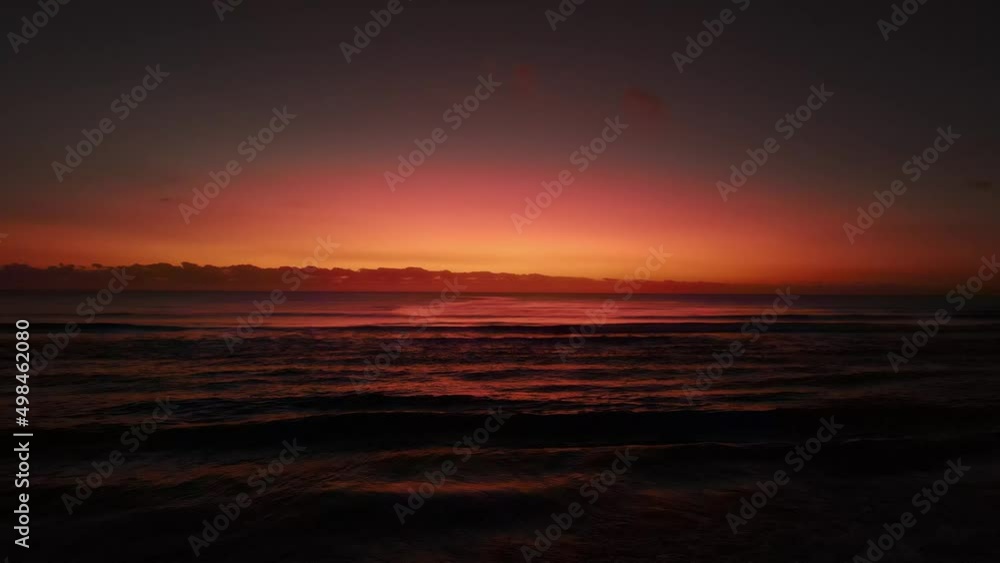 Glowing waves gently rolling across a saturated colourful sunrise ocean surface. Static drone view Glowing waves gently rolling across a saturated colourful sunrise ocean surface. Static drone view