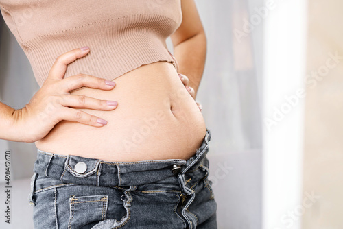 closeup belly fat woman checking her body in front of a mirror wearing jeans photo