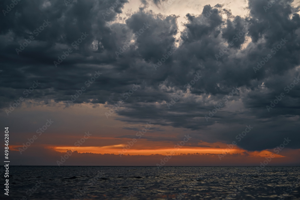 Beautiful sunset over the sea with gray dramatic clouds and orange sunset streak, dramatic sky