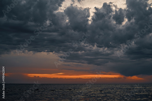 Beautiful sunset over the sea with gray dramatic clouds and orange sunset streak, dramatic sky