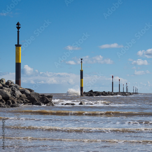 Waves crashing against the rocky breakwater with black and yellow cardinal posts marking the safe entrance to the bay, Sea Palling, Norfolk, UK