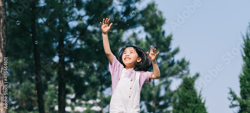 Image of Asian little girl playing with soap bubbles at park