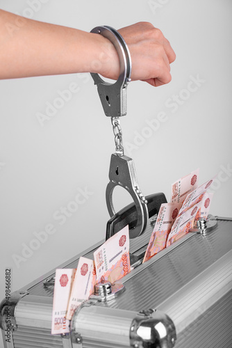 A man's hand handcuffed to a briefcase with money sticking out of it
