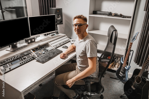 Man working in music studio using computer wearing glasses. Sound engineer working and mixing track. Programmer watching at display of it while listening music. Technology concept