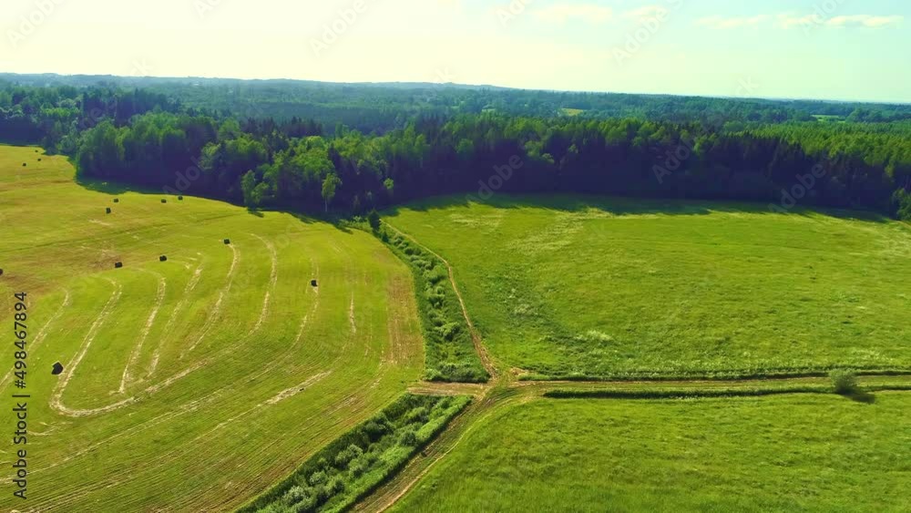 Aerial drone shot flying over a green field on a farm with hay bales are stacked on the field. Straw rolls on the grasslands at daytime. Aerial drone shot flying over a green field on a farm with hay bales are stacked on the field. Straw rolls on the grasslands at daytime.